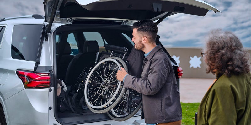 man putting wheelchair in trunk of Chevy Traverse